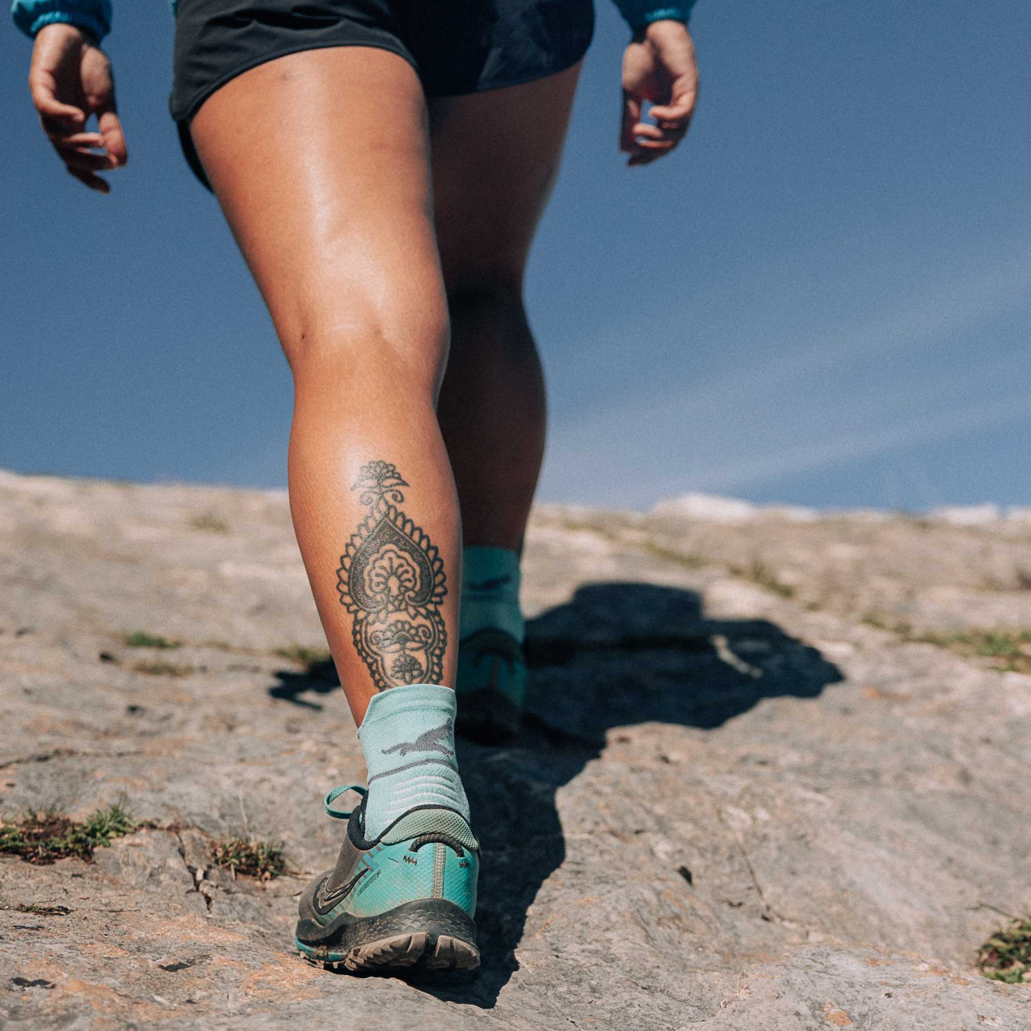 Close up of a persons legs as they are walking up a rocky hill. They are wearing bright blue socks and running shoes.