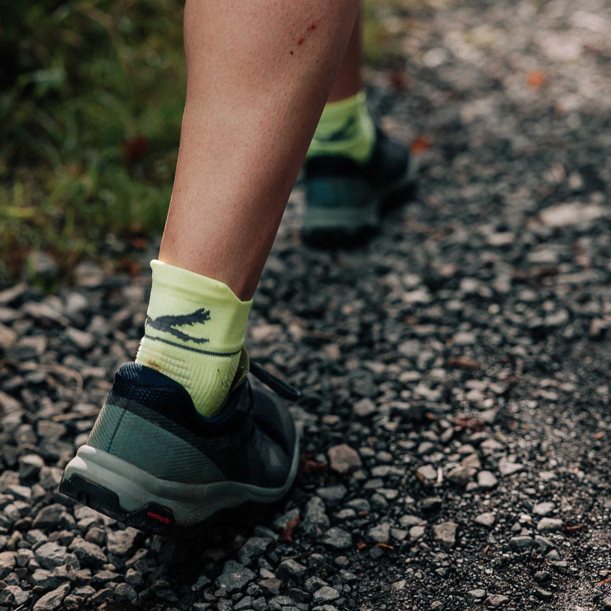 Close up of a persons lower legs walking on a gravel path. They are wearing bright yellow socks and running shoes.