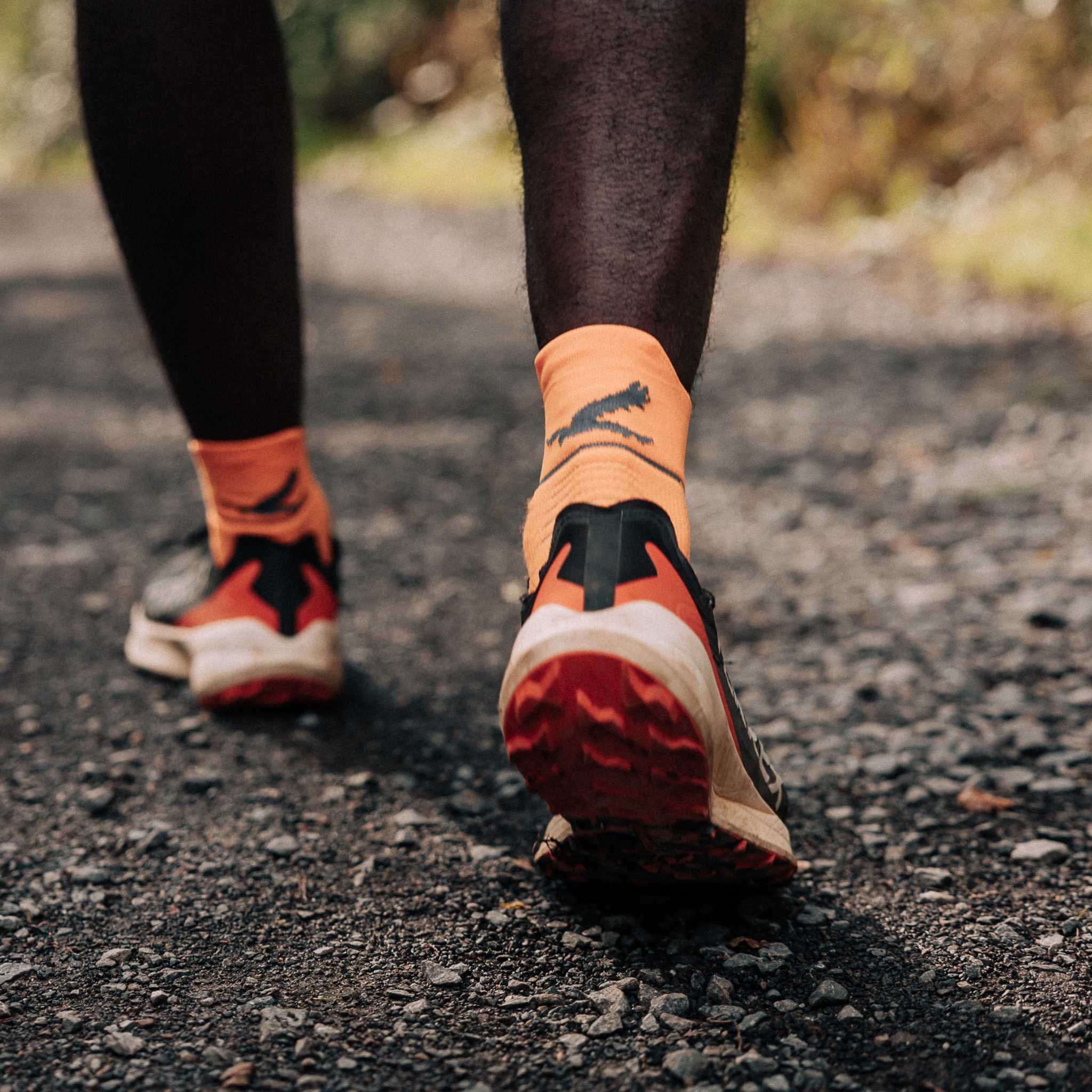 Close up of a persons lower legs walking on a gravel path. They are wearing bright orange socks and running shoes.