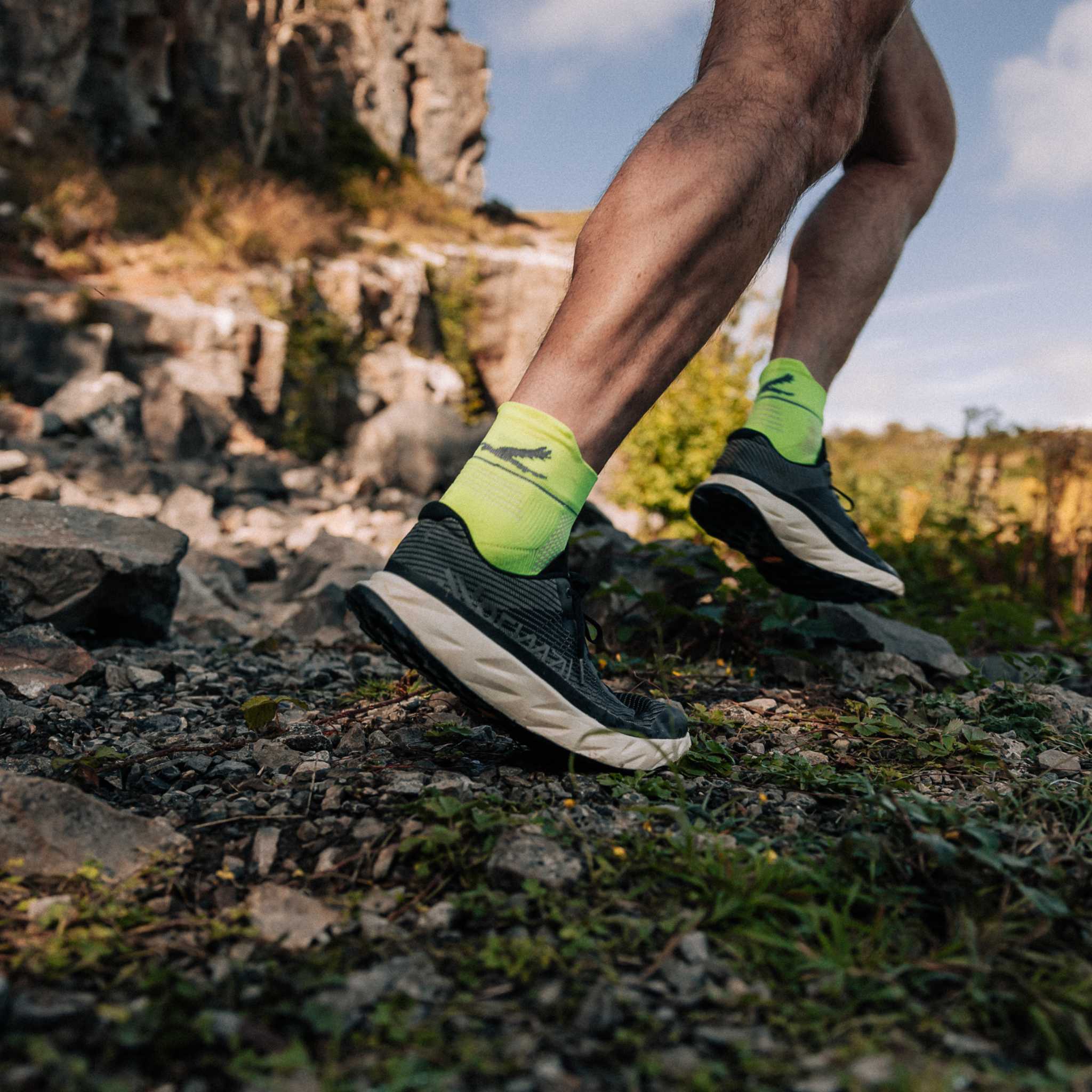 Close up of a persons lower legs running on a gravel path. They are wearing bright yellow socks and running shoes.