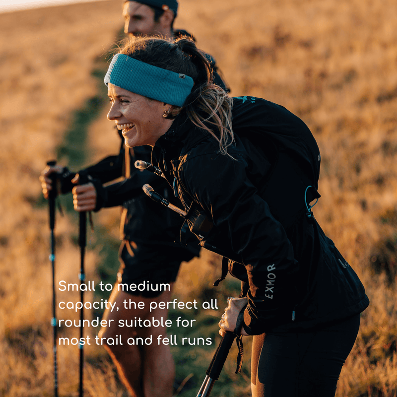 A man and a woman in the countryside, both wearing a running hyydration vest. They are laughing.  