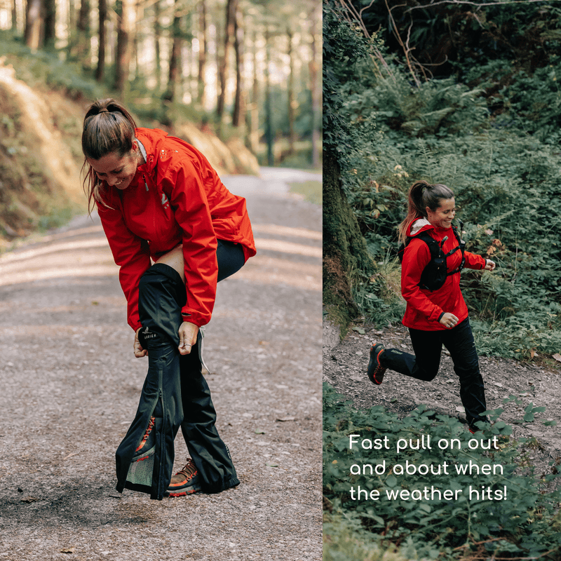 A woman stood in the forest, pulling on her waterproof trousers. She is smiling. 
