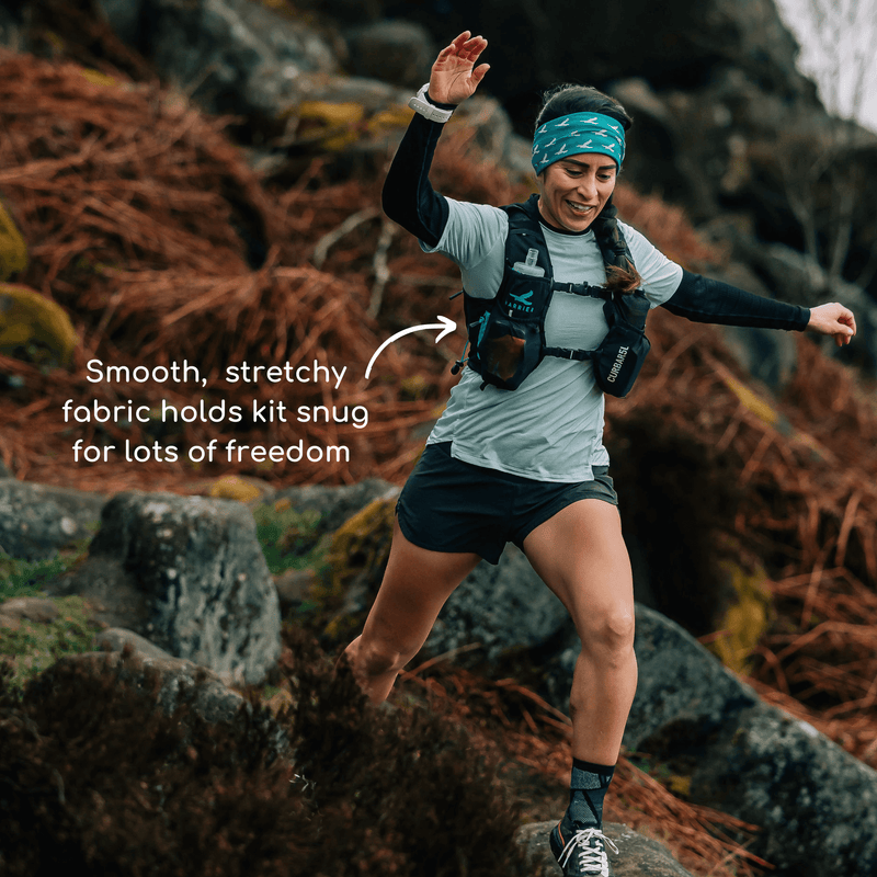 A woman wearing a hydration vest running in the countryside. She is smiling. 