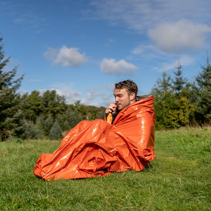 A man in a field demonstrating using the survival bag and whistle.