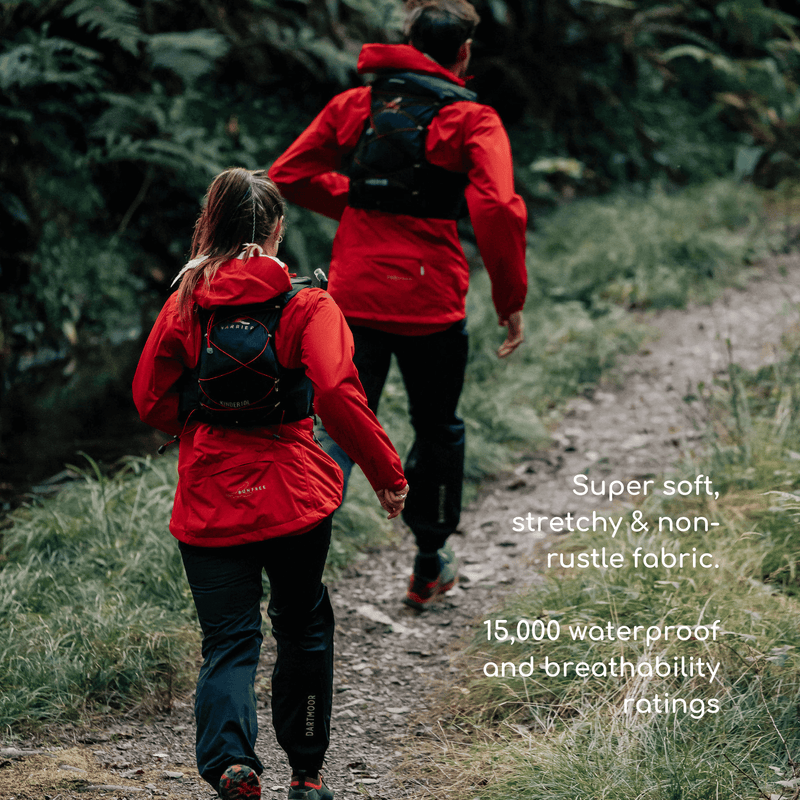 A man and a woman running in the forest. They are wearing a waterproof jacket and trousers. 