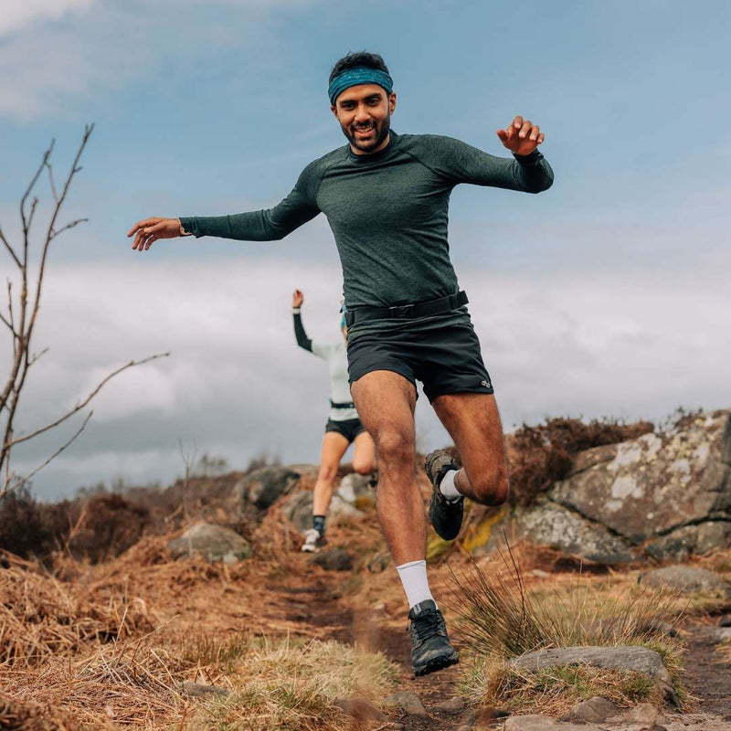 A man wearing a waist bag running in the countryside, he is smiling. 